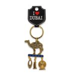 Gold-tone Dubai souvenir keychain featuring an intricately patterned filigree camel standing on a blue "Dubai" bar with dangling charms of the Burj Al Arab and Ain Dubai ferris wheel.