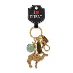 Gold-tone Dubai souvenir keychain featuring a large filigree camel charm, a black and gold Burj Al Arab building charm, and a teal circular charm with a gold palm tree.
