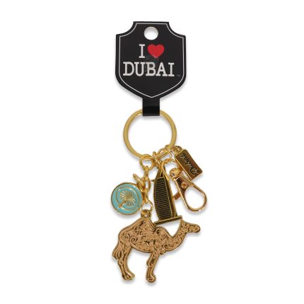 Gold-tone Dubai souvenir keychain featuring a large filigree camel charm, a black and gold Burj Al Arab building charm, and a teal circular charm with a gold palm tree.