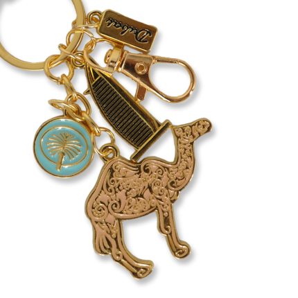 Gold-tone Dubai souvenir keychain featuring a large filigree camel charm, a black and gold Burj Al Arab building charm, and a teal circular charm with a gold palm tree.
